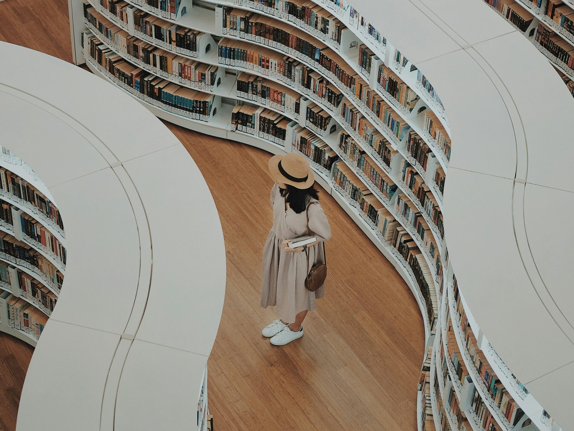A reader holding books between curved library shelves