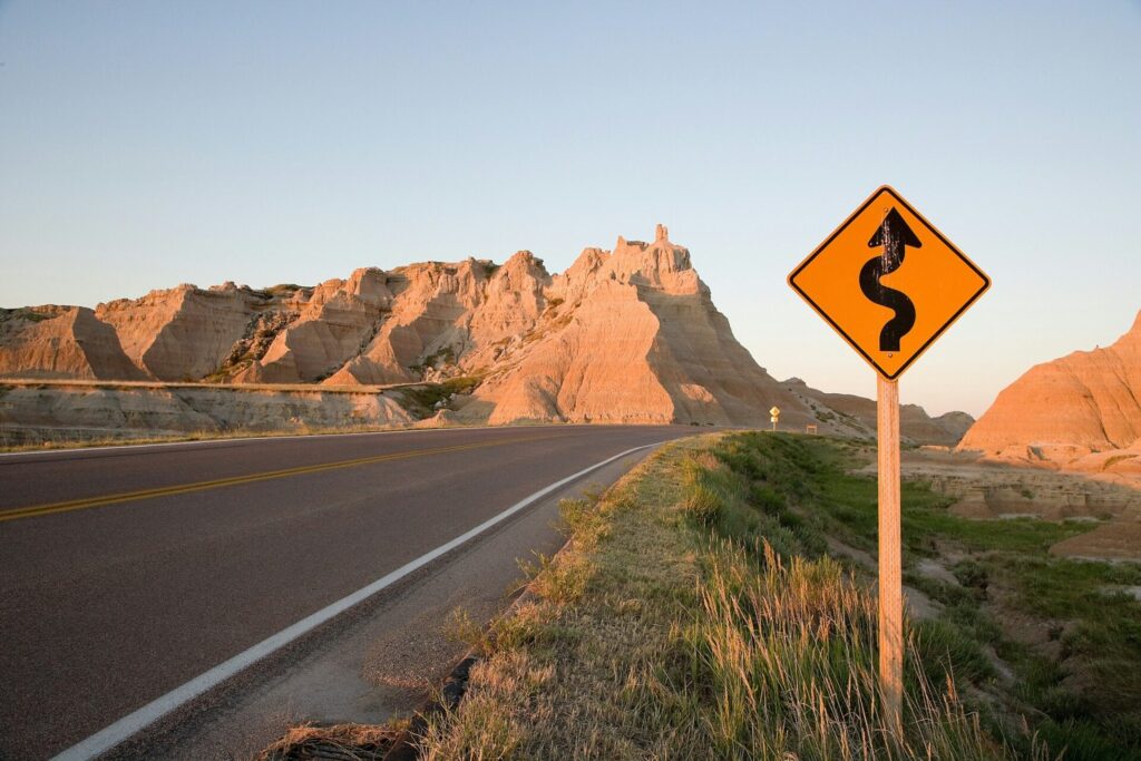 A winding-road warning sign beside a road through a rocky landscape